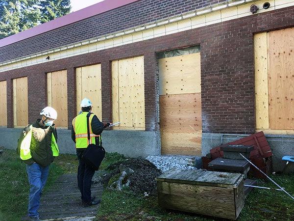 工人们站在一座砖房前，砖房上有窗户和门的洞, 但它们是用胶合板填充的